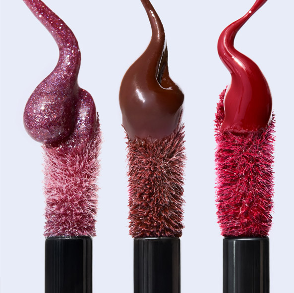 Three lip gloss applicators with product swirls on a grey background 